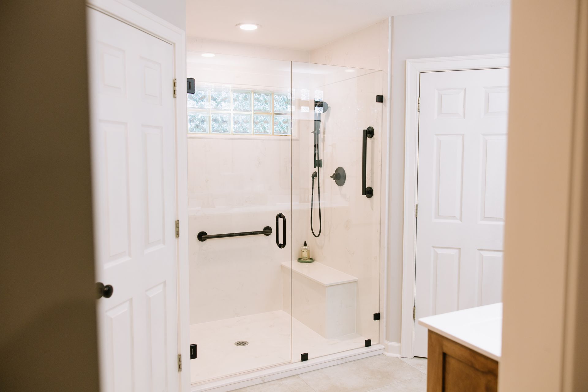 Bright bathroom with a glass walk-in shower, white tile, and a wooden vanity edge.