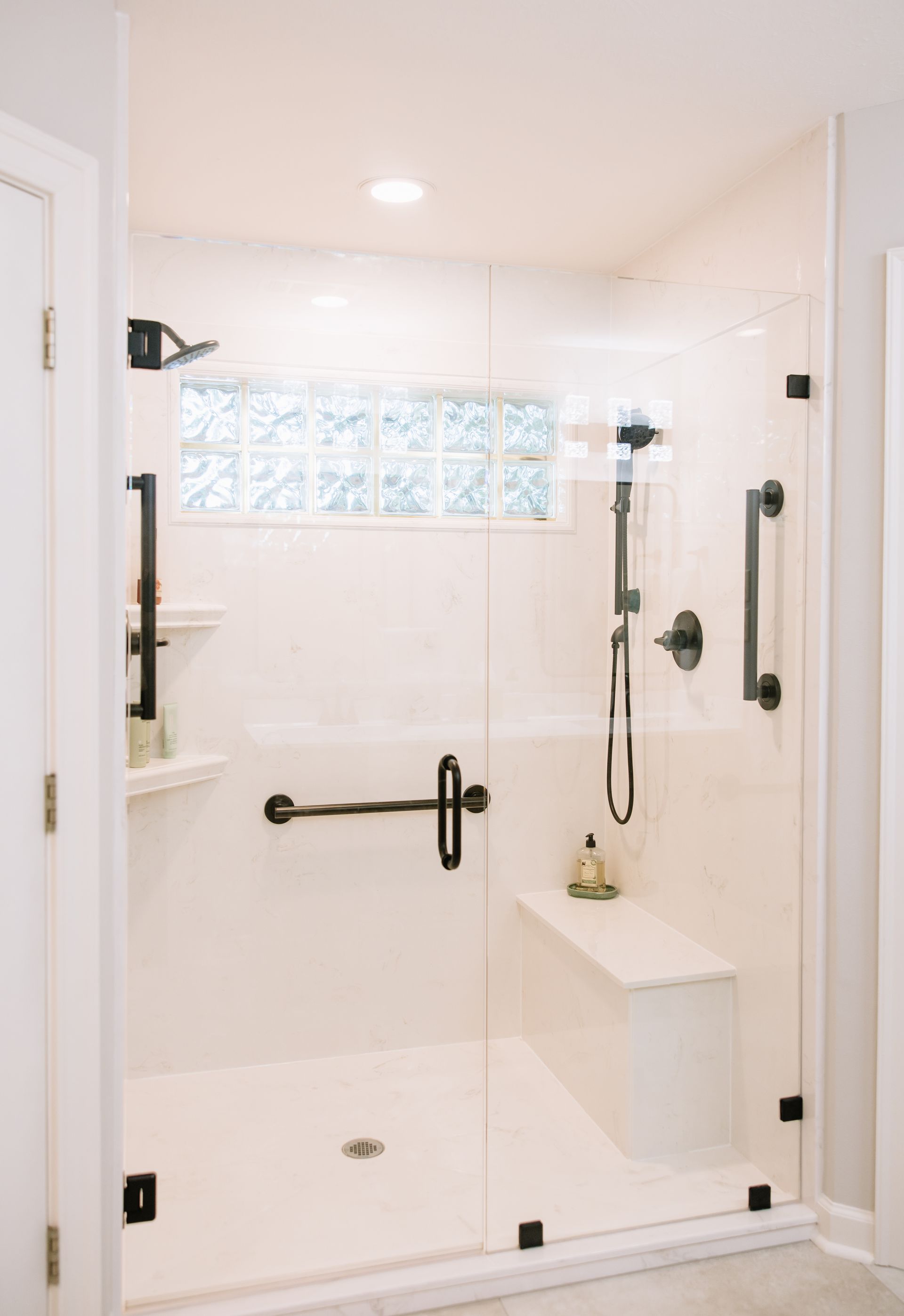 Accessible white shower stall with grab bars, bench seat, and handheld showerhead