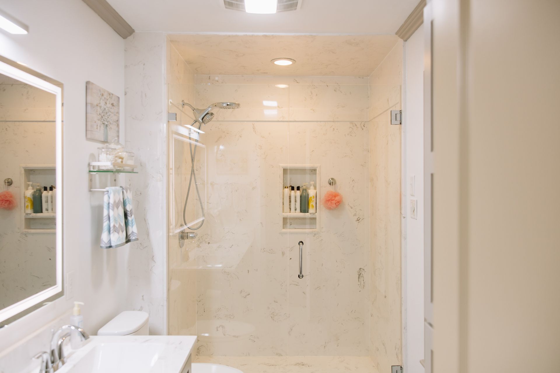 Bright cream bathroom with glass shower, mirror, and white sink.