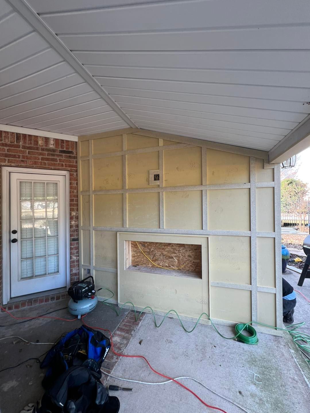 Partially finished wall in a covered patio, with exposed framing, insulation, and tools on the floor