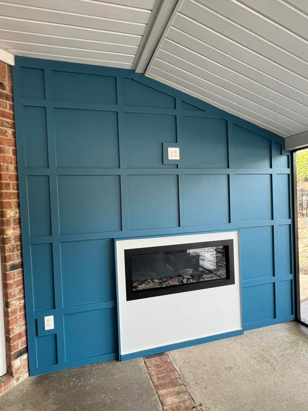 Blue paneled wall with a modern fireplace insert under a sloped white ceiling on a covered patio