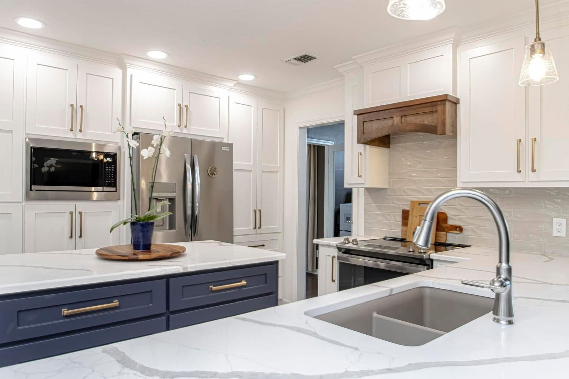 Bright modern kitchen with white cabinets, blue island, stainless appliances, and marble countertops