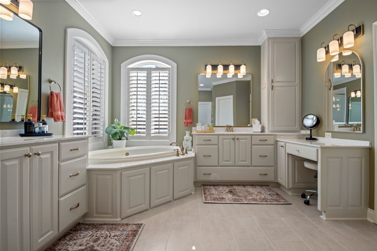 Spacious gray bathroom with double vanities, bathtub, arched window, and wall sconces