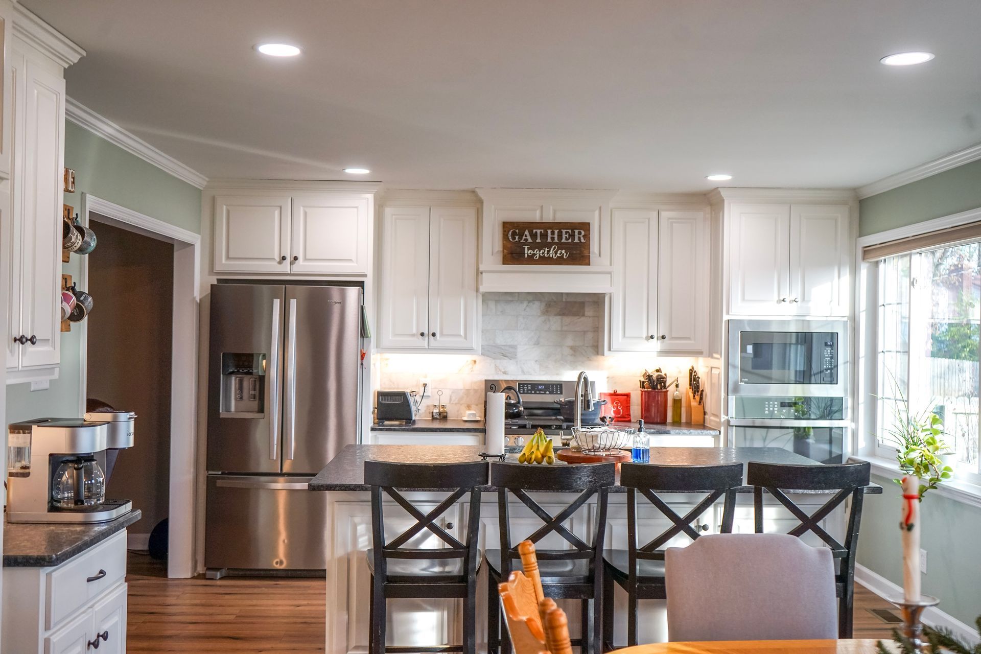 Bright modern kitchen with stainless fridge, white cabinets, island stools, and a window view