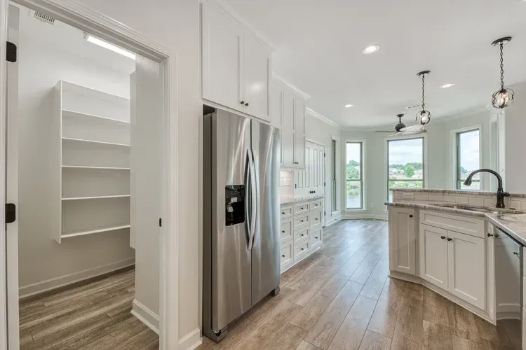 Bright white kitchen with stainless steel fridge, island, and pantry closet opening to a hallway