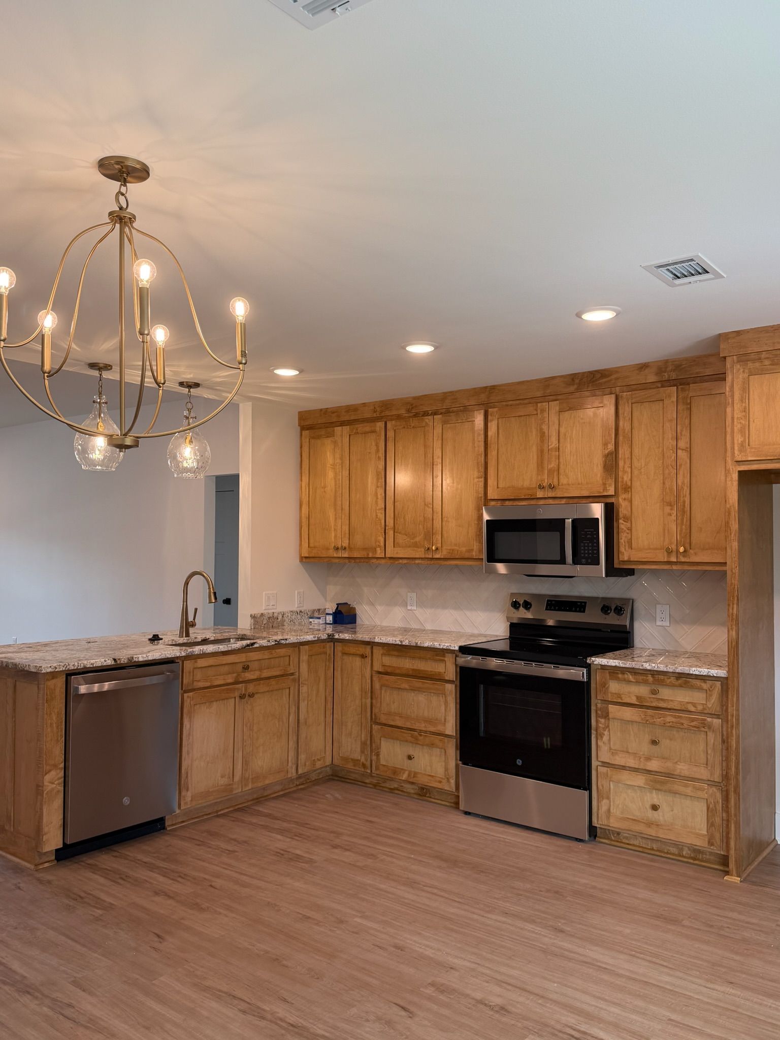 Modern kitchen with wood cabinets, stainless appliances, chandelier, and wood-look flooring