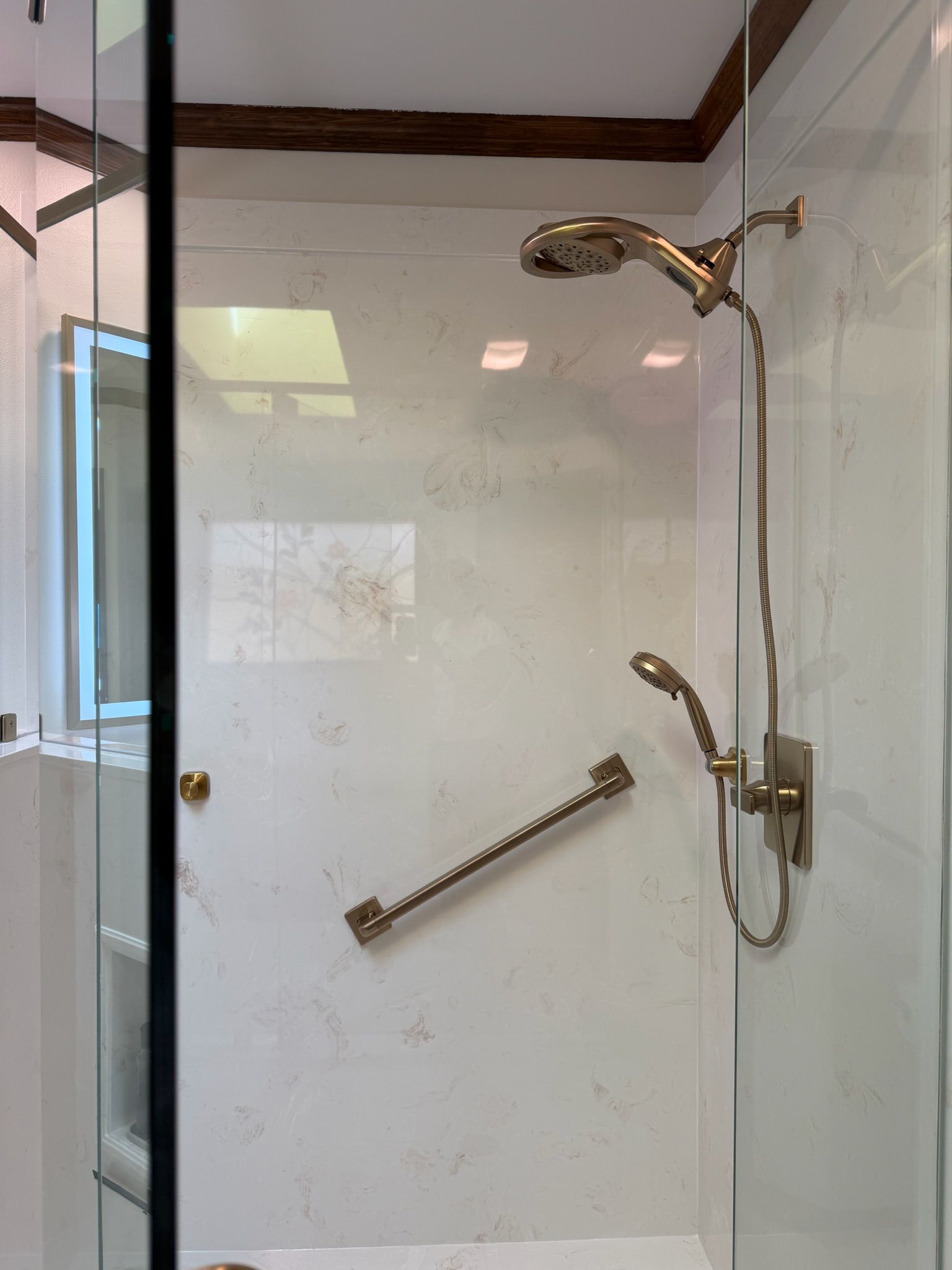 Glass-enclosed shower with white tile, grab bar, and handheld showerhead.