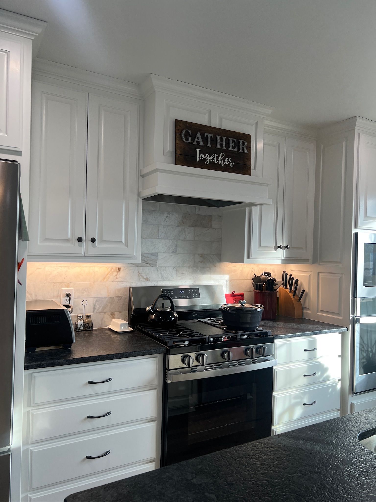 Bright white kitchen with black stove, cabinets, and speckled countertop under a decorative sign.