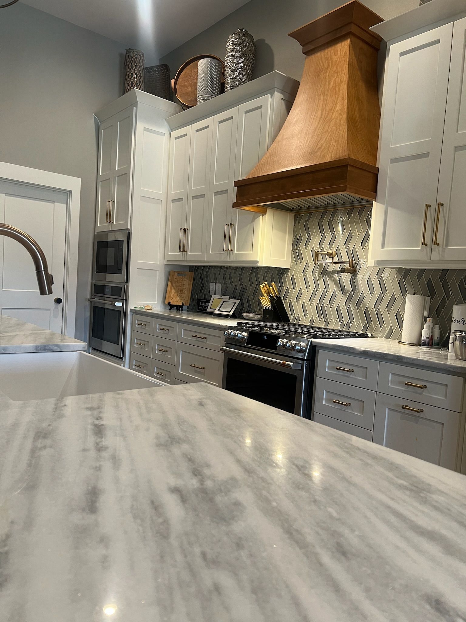 Modern kitchen with white cabinets, gray island countertop, stainless appliances, and copper range hood