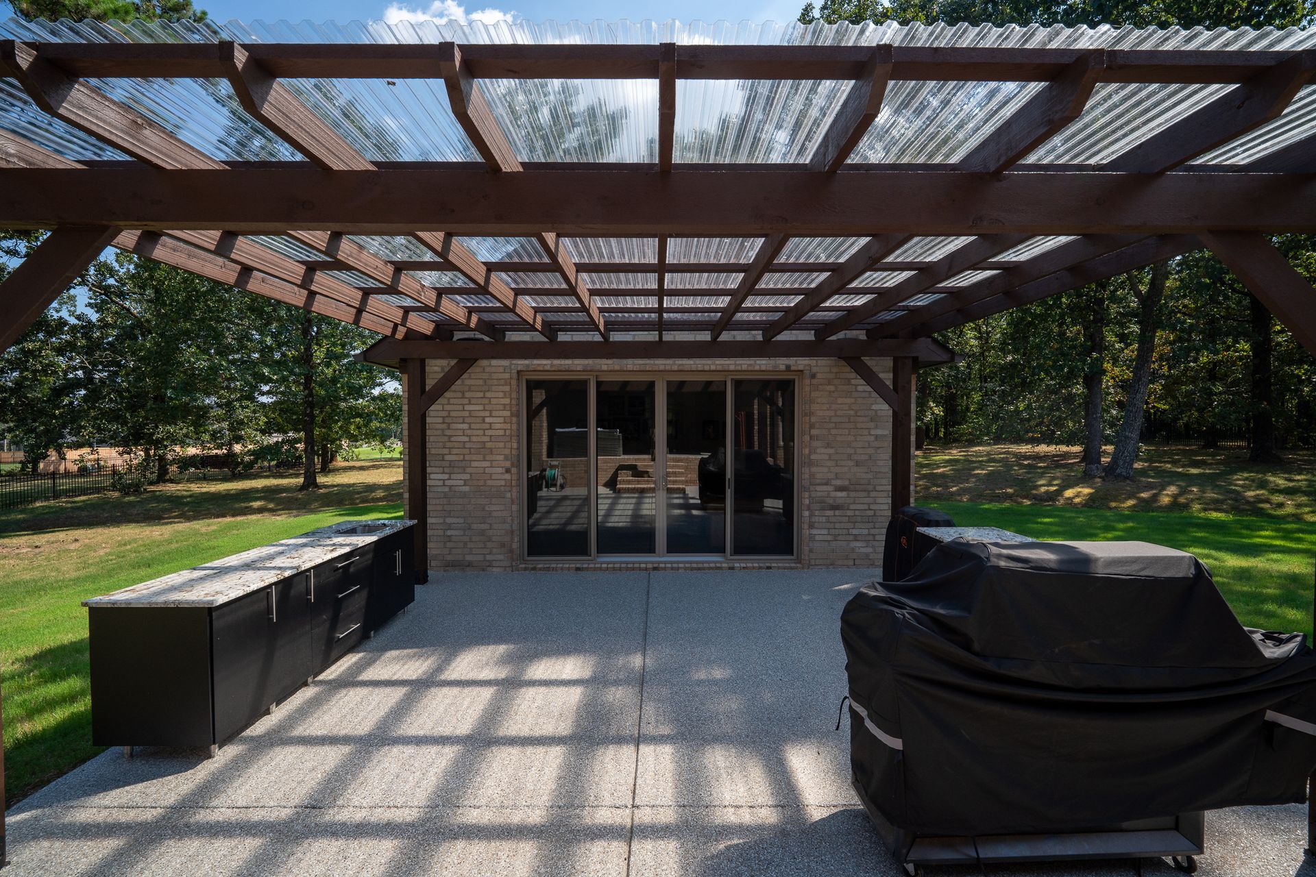 Outdoor patio with a wooden pergola, table and chairs, and a covered grill in front of a small building