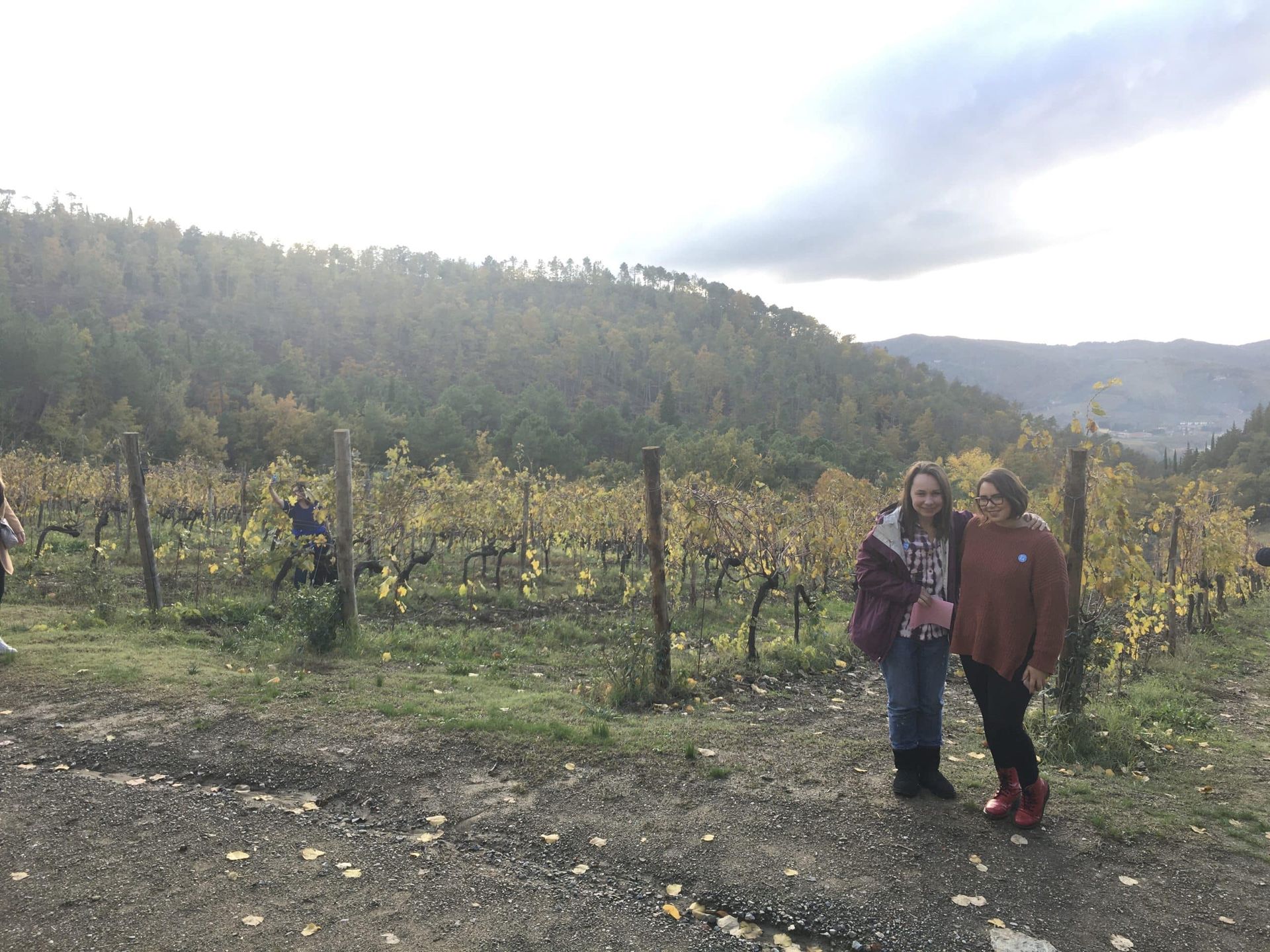 Two people standing in a vineyard with hills and cloudy sky in the background