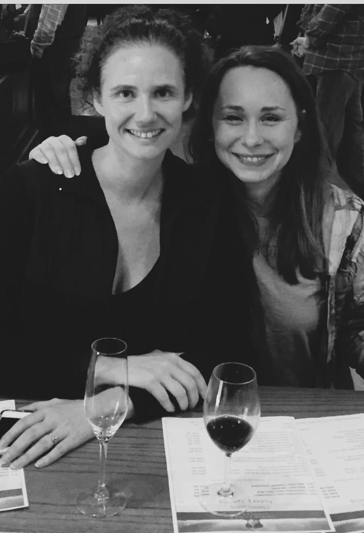Two smiling people seated at a restaurant table with wine glasses and a menu.