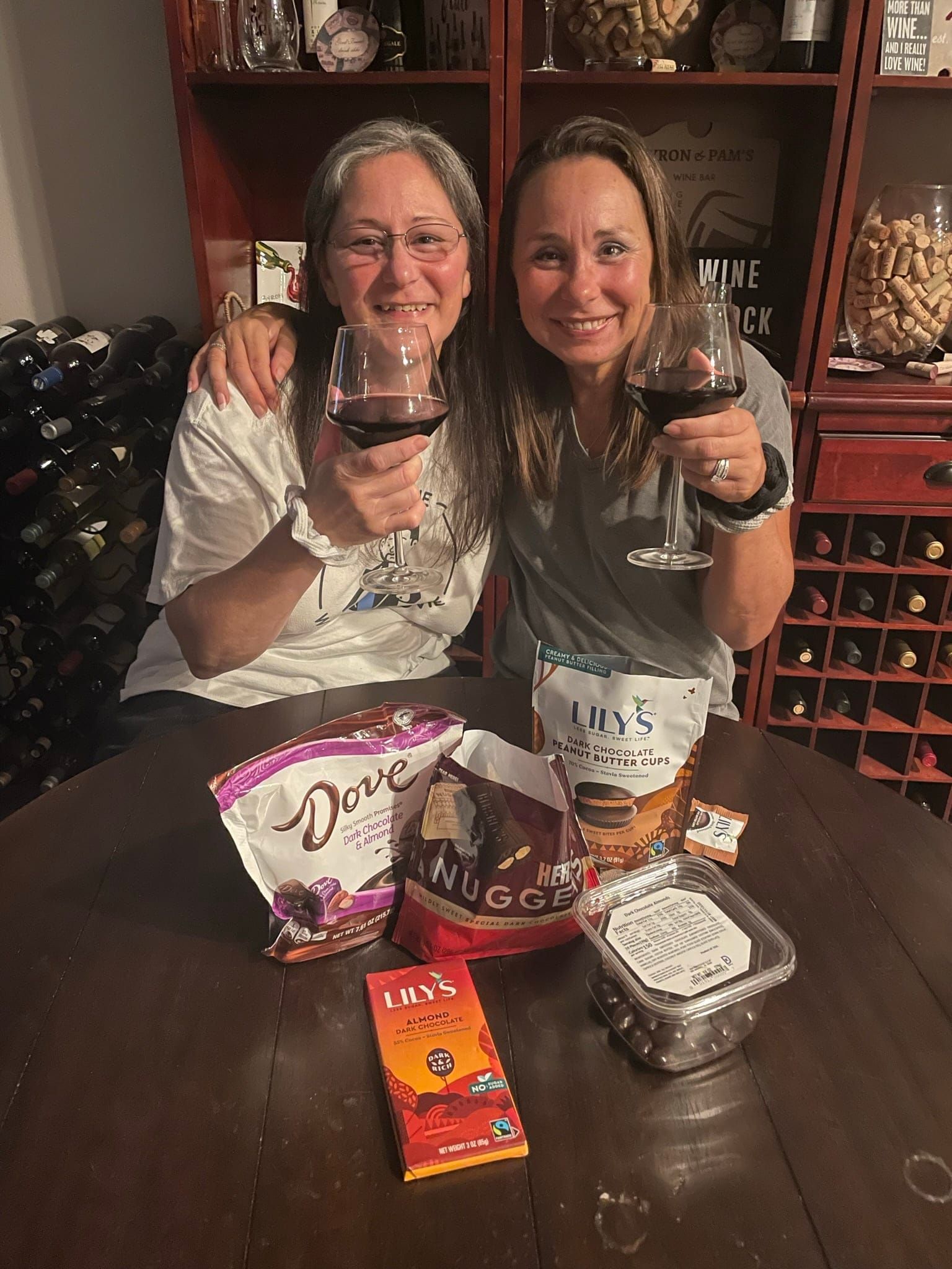 Two people smiling and holding wine glasses at a restaurant table with snacks and wine bottles