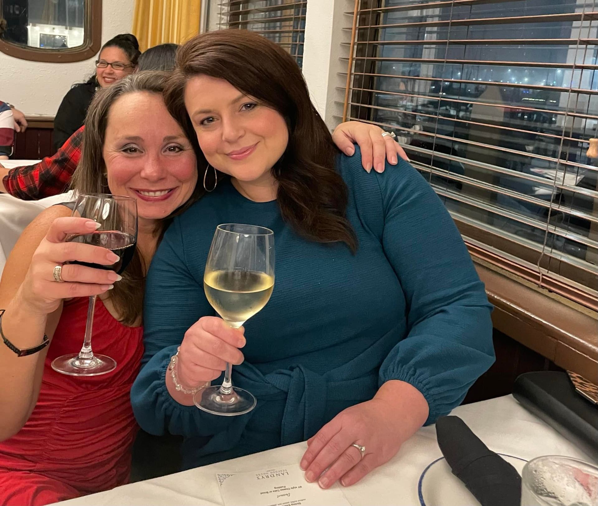 Two women smiling at a restaurant table, each holding a glass of wine.