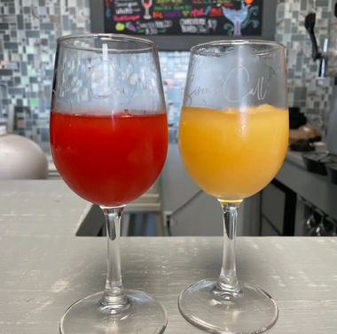 Two wine glasses on a counter, one filled with red drink and one with orange drink.
