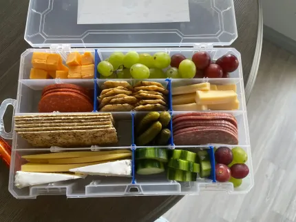 Open tackle box filled with assorted crackers, fruits, vegetables, cheese, and dip cups