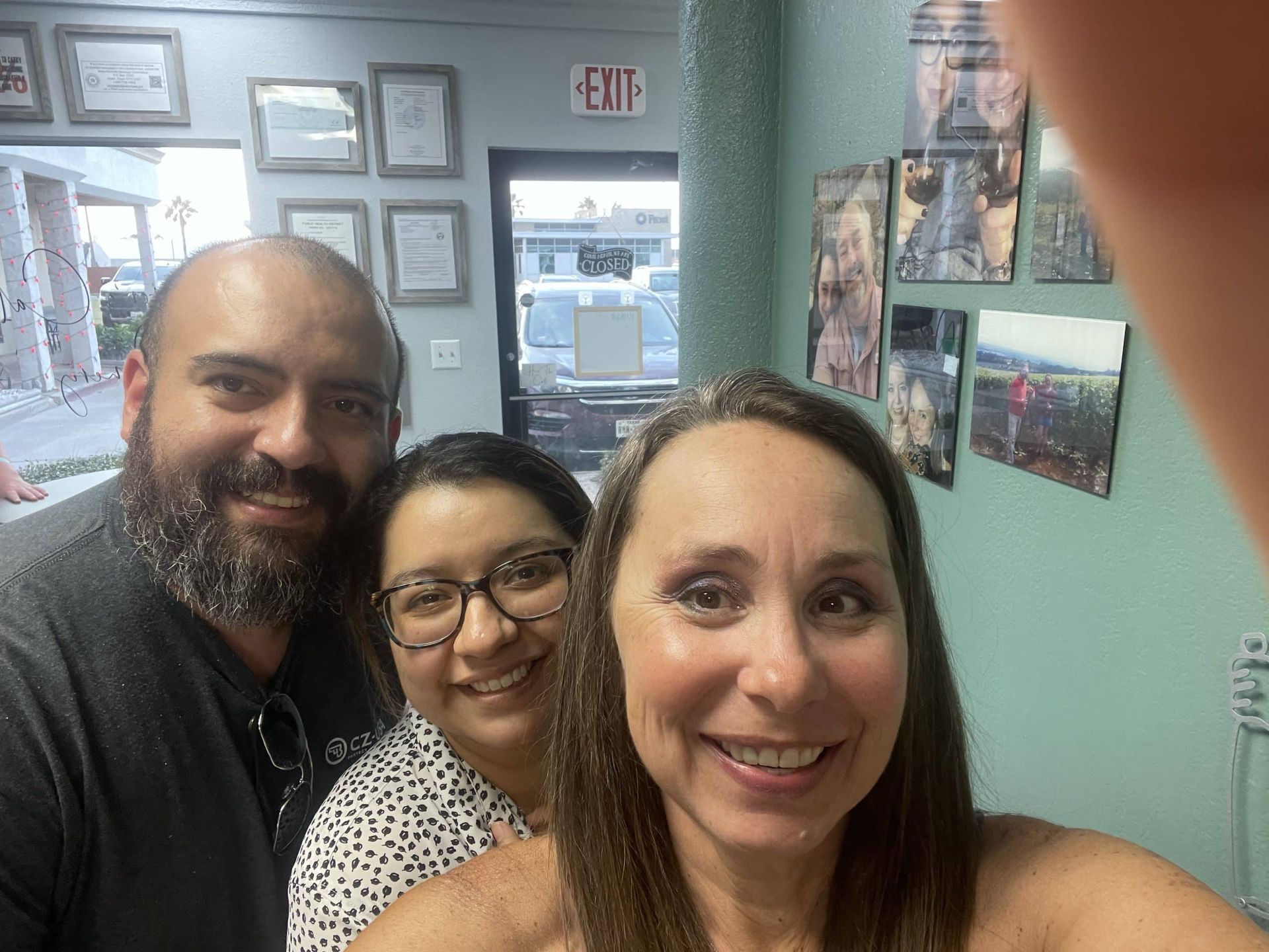 Three smiling people taking a selfie indoors in a framed art gallery hallway