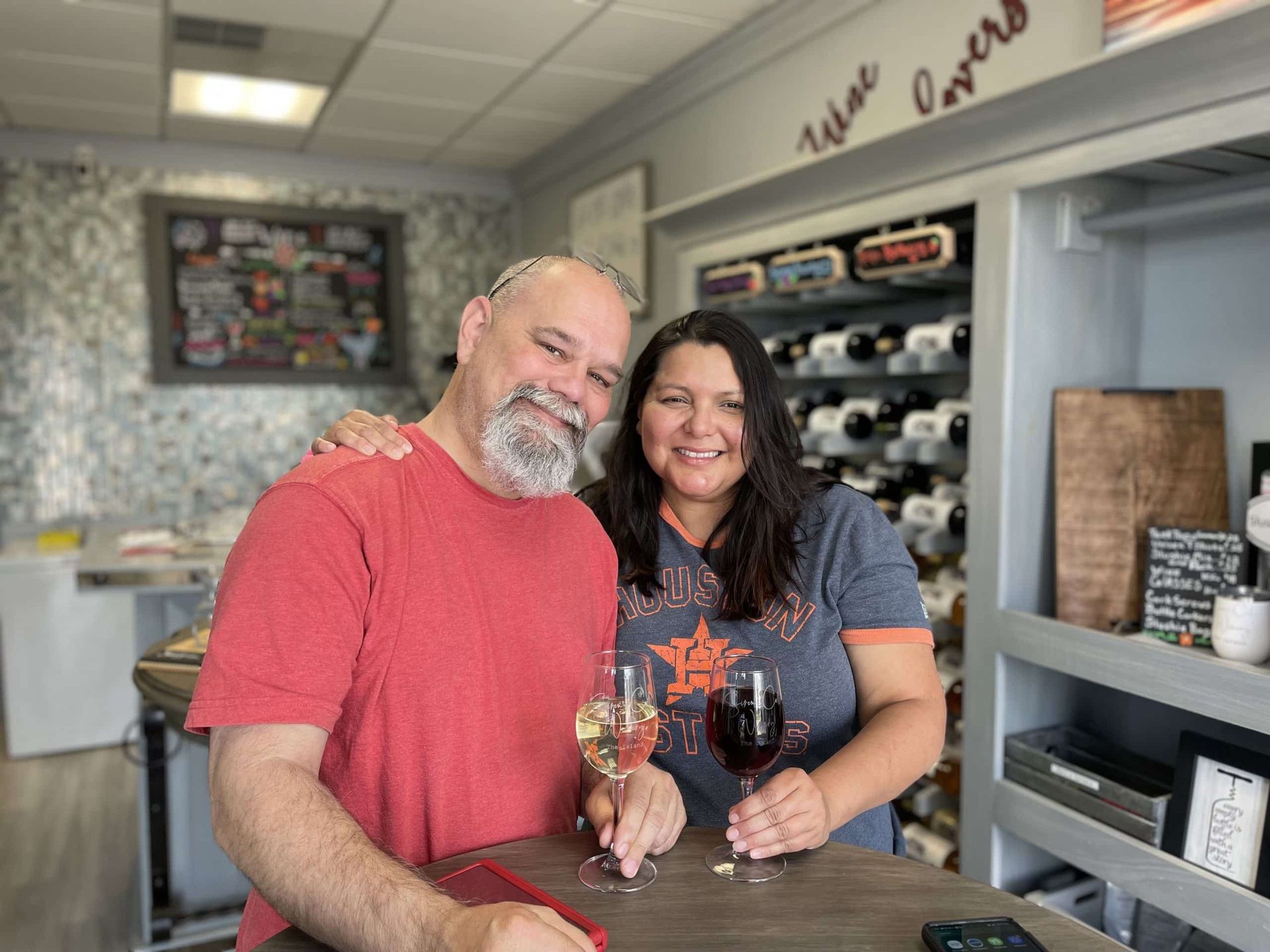 Two smiling adults posing behind a counter in a shop with shelves and wall decor