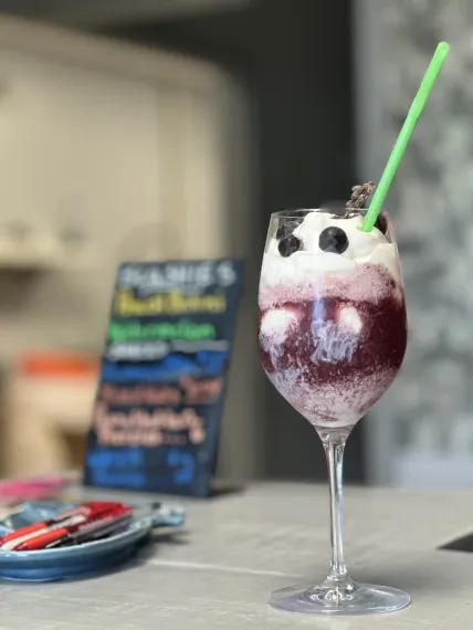 Purple iced drink with whipped cream, blueberries, and a green straw on a table