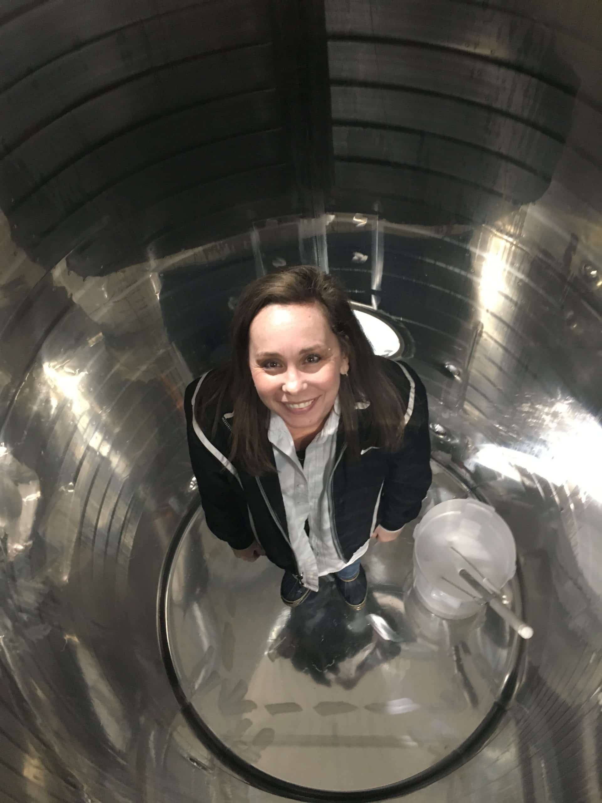 Person smiling inside a clear cylindrical tunnel, viewed from above.
