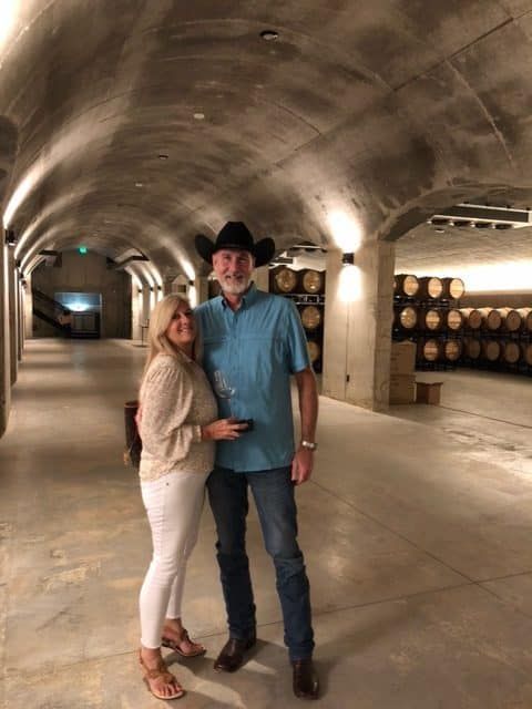Couple posing in a wine cellar beside stacked barrels, one in a cowboy hat.