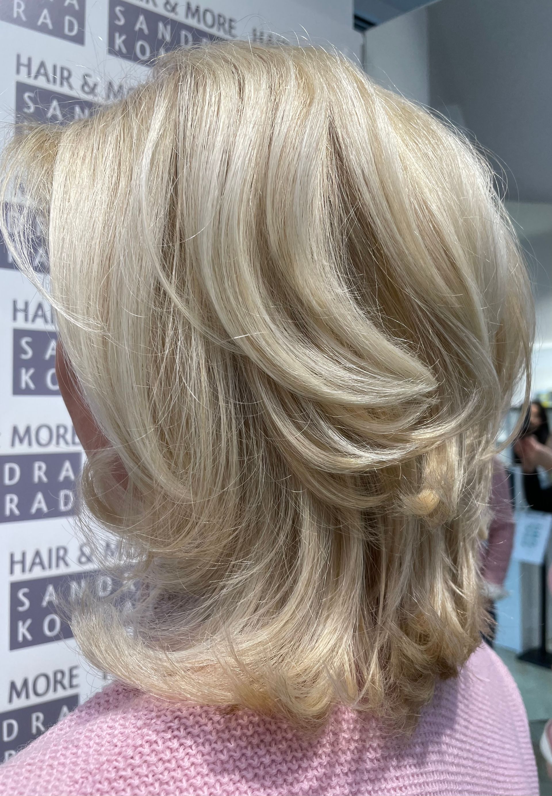 Blondes, glitzerndes Haar im Stufenschnitt. Salonhintergrund mit Text.