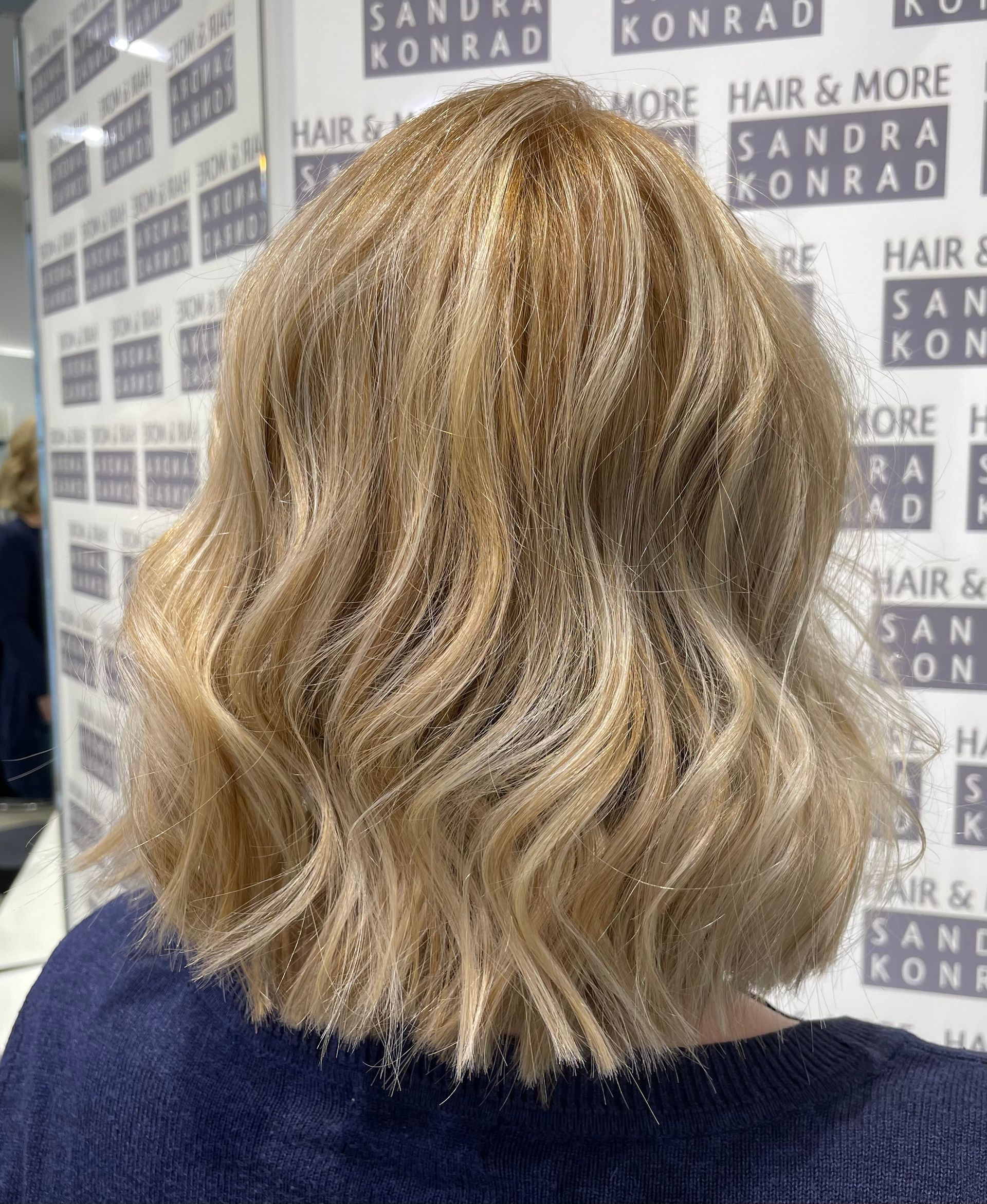 Wellige, blonde Bobfrisur einer Frau mit Glitzer. Hintergrund: Friseursalon.