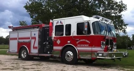 A red and white fire truck is parked in a grassy field