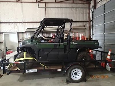 A green kawasaki utility vehicle is on a trailer in a garage.