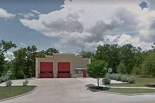 A fire station with red doors is surrounded by trees and grass.