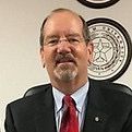A man in a suit and tie is sitting in front of a wall.