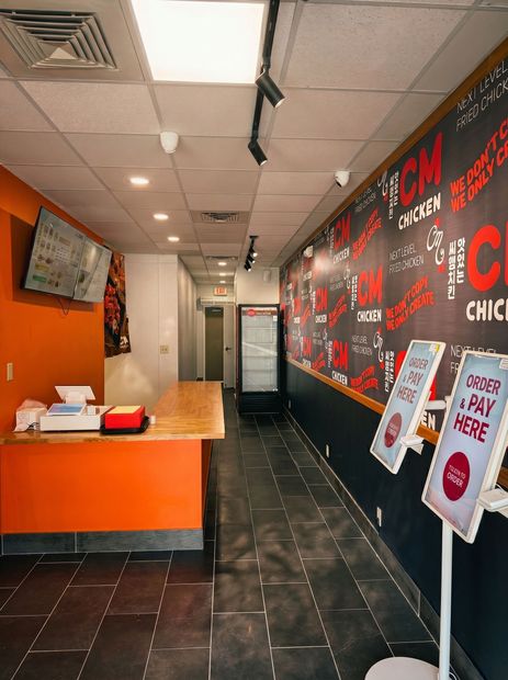 Orange-and-black fast-food restaurant interior with counter, menu wall, and tiled floor hallway