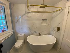 Bright minimalist bathroom with white tub, double vanity, large windows, and gold accents