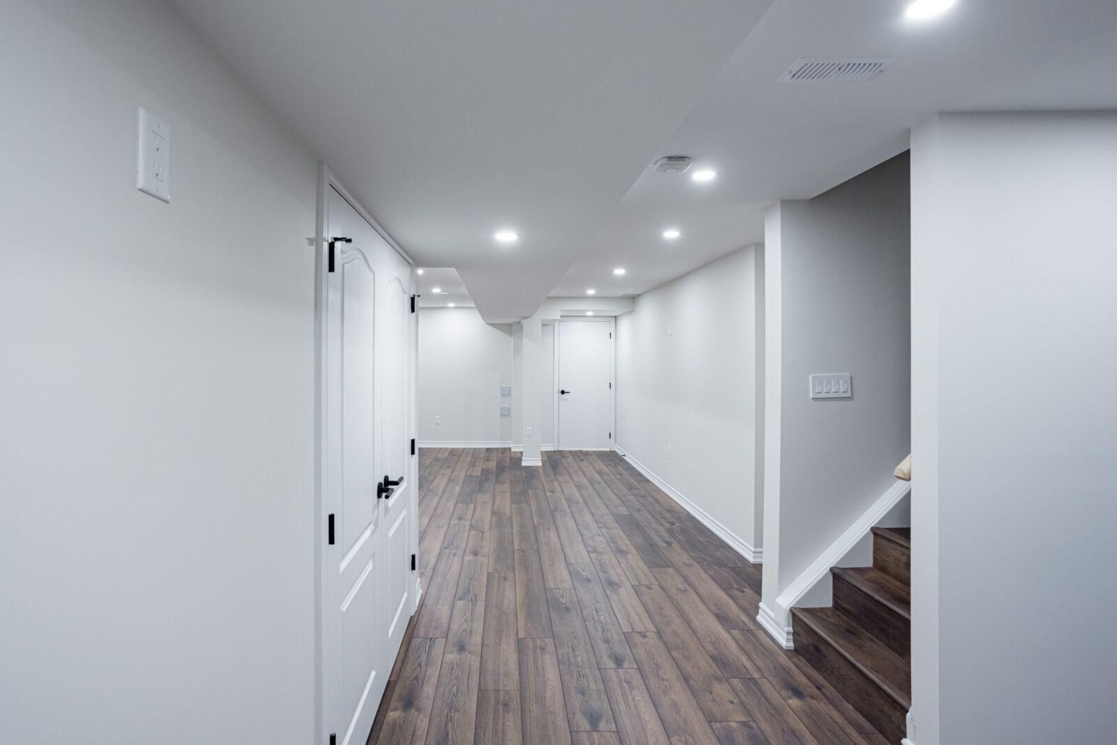 Empty modern hallway with white walls, wood-look flooring, recessed lights, and stairs on the right