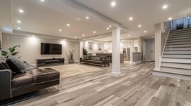 Spacious modern basement living room with sectional sofa, wall TV, dining area, and staircase