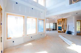 Bright unfinished modern room with large windows, high ceilings, and exposed construction materials inside a home