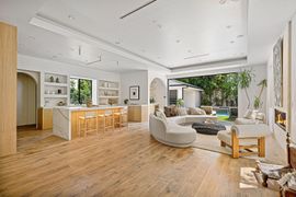 Bright open-plan living room with white sofas, wood floors, kitchen island, and large glass doors to a garden