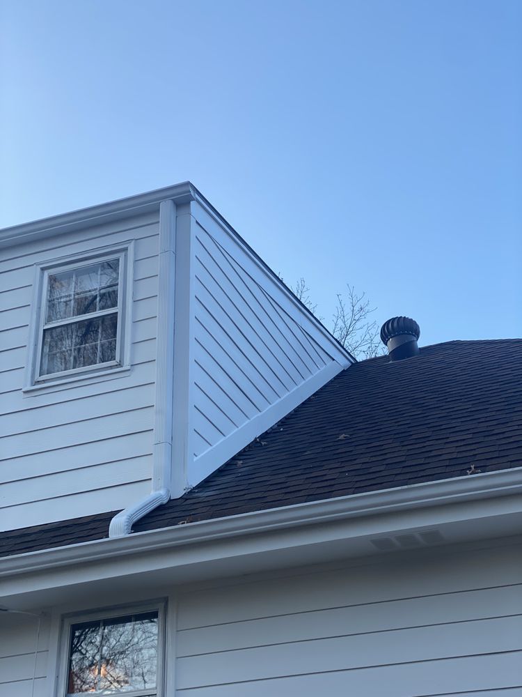 White house roof with dormer window and chimney against a clear blue sky