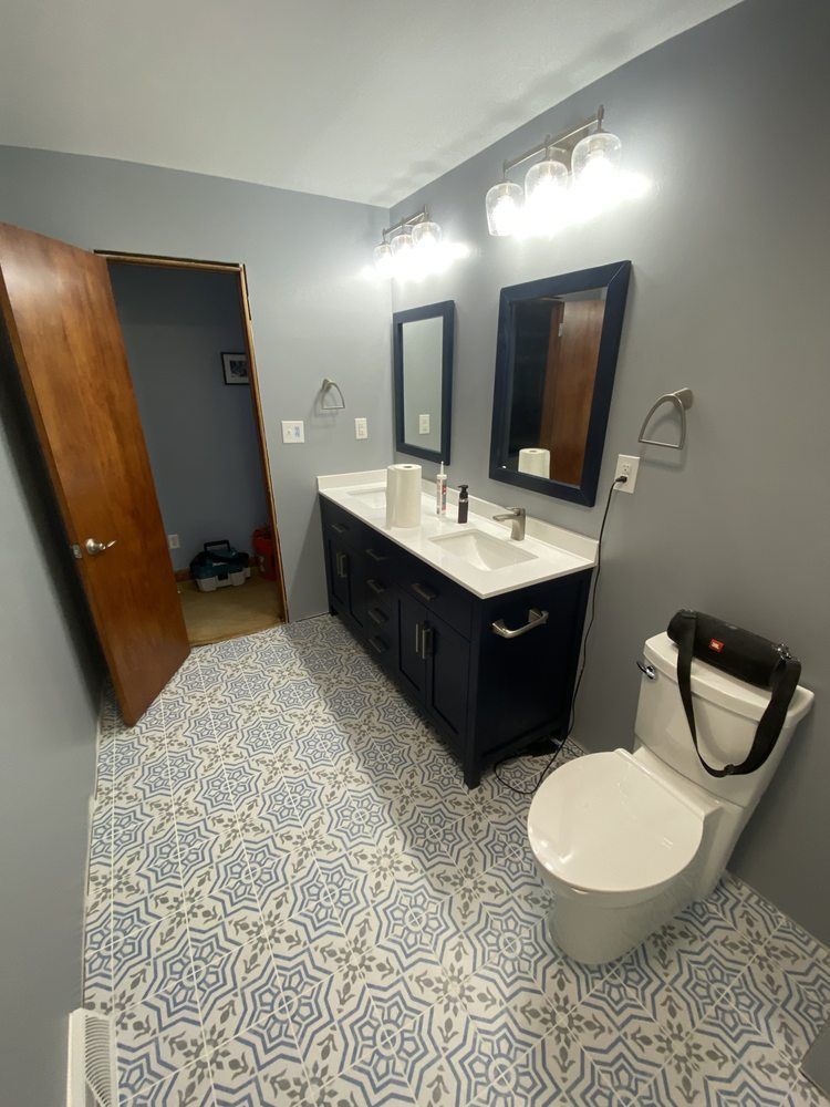 Modern bathroom with gray walls, patterned tile floor, black vanity, sink, mirror, and toilet near an open door