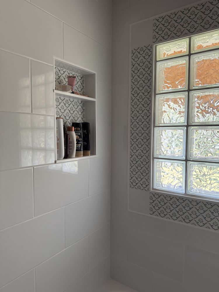 White tiled shower with recessed shelves and a frosted glass block window with patterned trim.