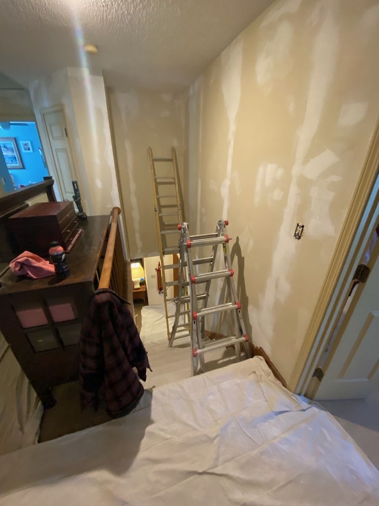 Hallway under renovation with drywall patches, ladders, tools, and a drop cloth on the floor.
