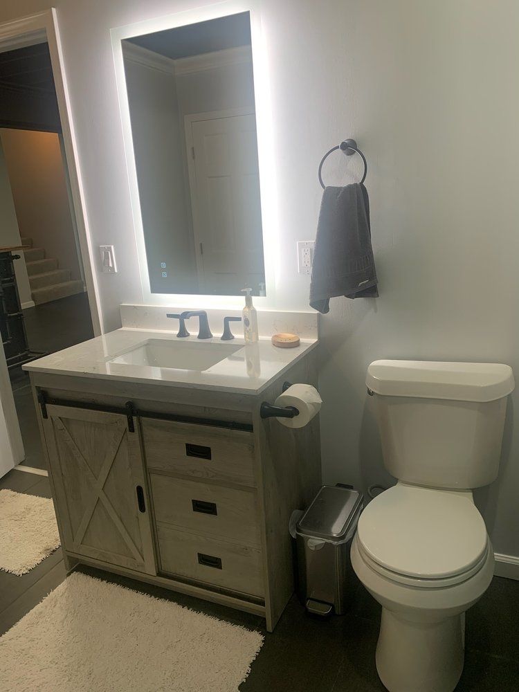 Bathroom with vanity, lit mirror, towel ring, and toilet.