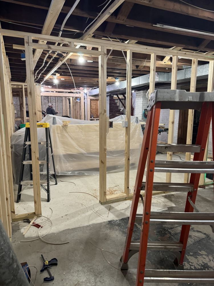 Basement renovation with exposed framing, ladders, and covered furniture under construction