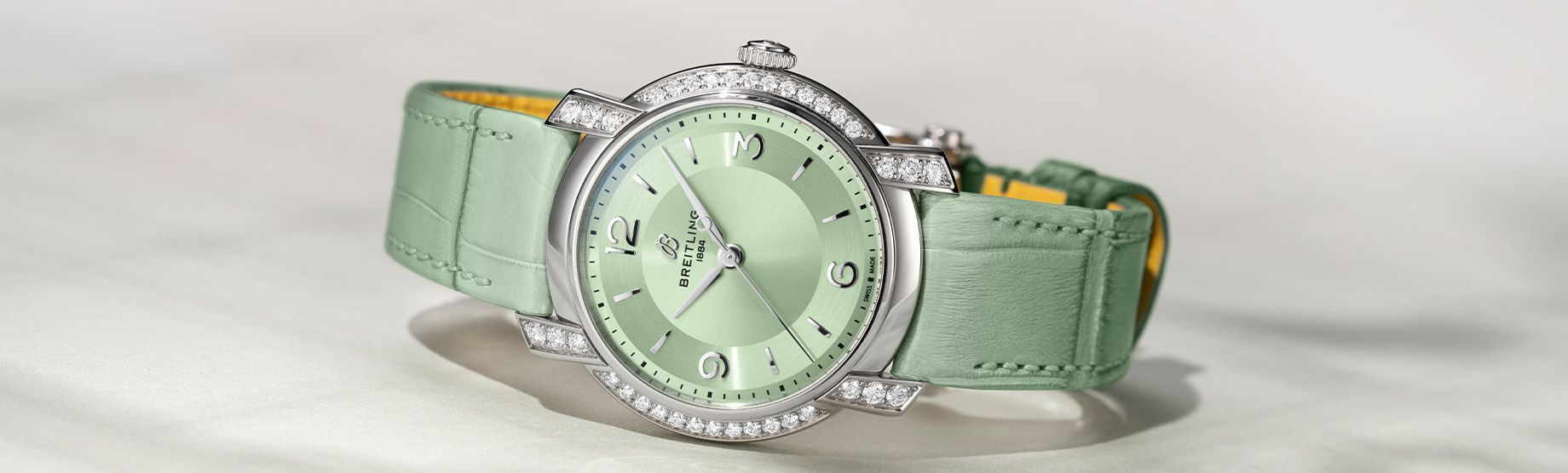 Mintgroen polshorloge met een met edelstenen bezette lunette en bijpassende band op een lichte achtergrond.
