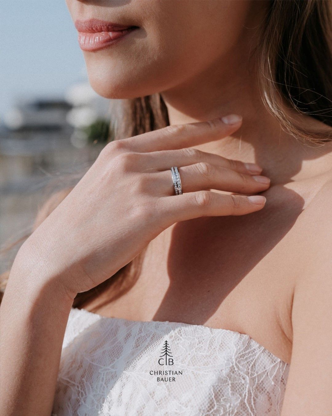 Een persoon in een witte kanten jurk legt haar hand op haar nek en toont een met diamanten bezette ring om haar ringvinger.