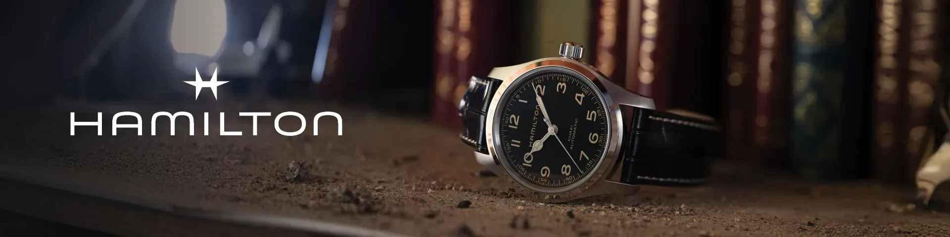 Hamilton horloge met zwarte wijzerplaat en zilverkleurige kast met een warme achtergrond bij kaarslicht.