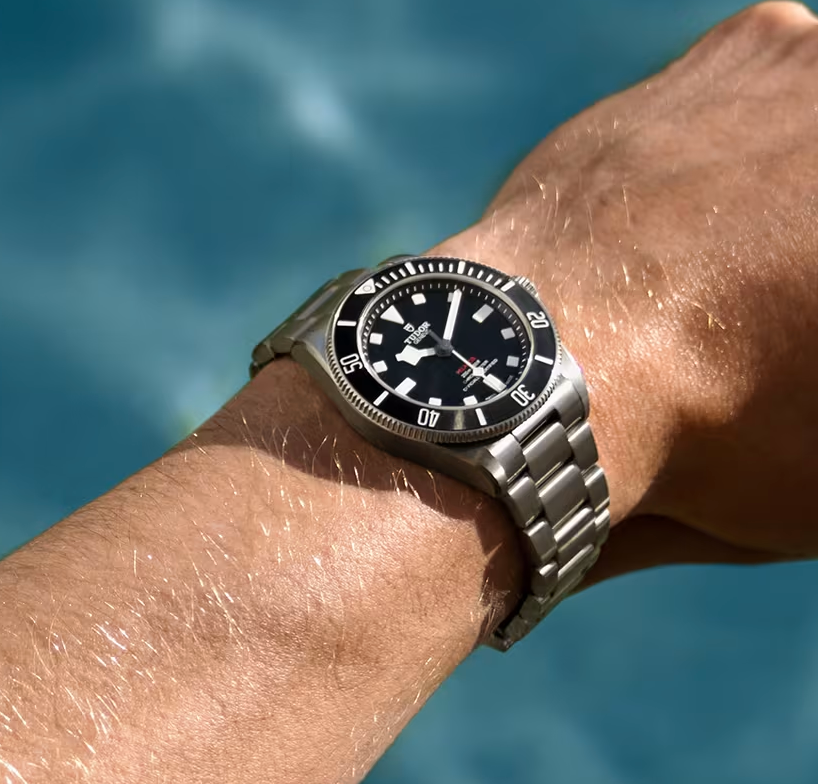 Close-up van een zilveren duikhorloge om een ​​pols tegen een achtergrond van blauw water.