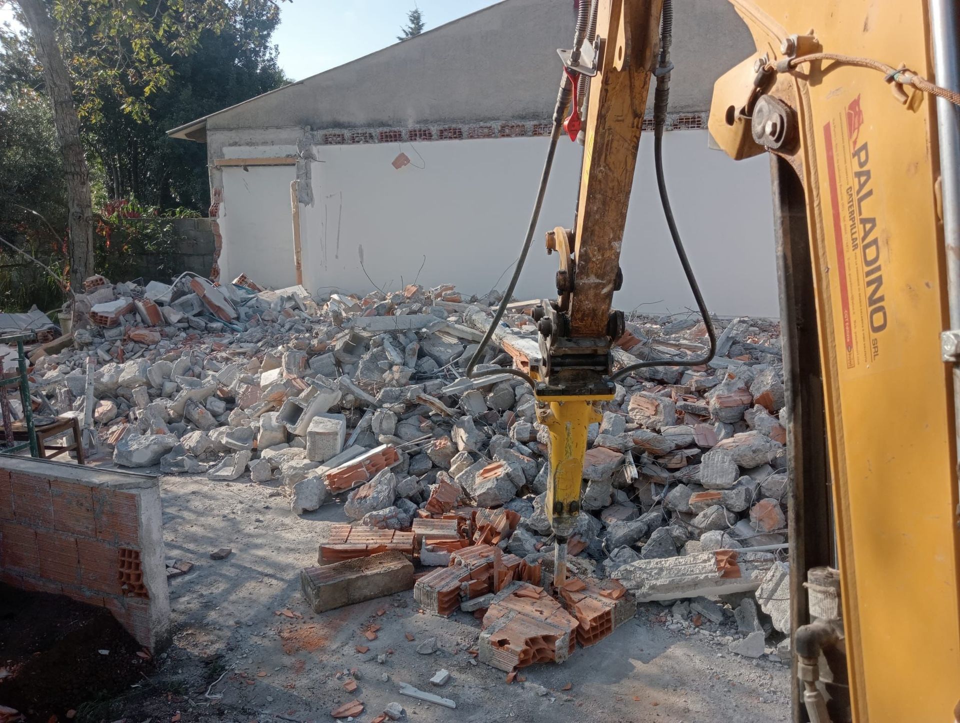 Un escavatore giallo sta demolendo un edificio con un martello attaccato.