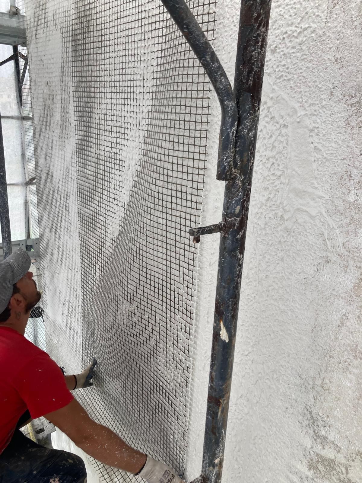 Un uomo è seduto su un'impalcatura e lavora su un muro.
