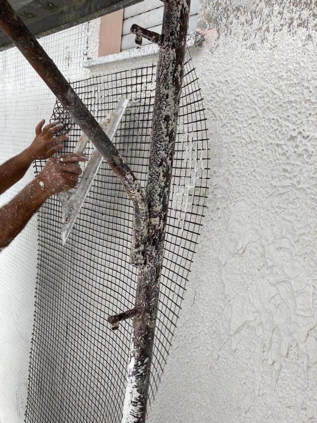 Un uomo sta dipingendo un muro con una cazzuola mentre è in piedi su un'impalcatura.